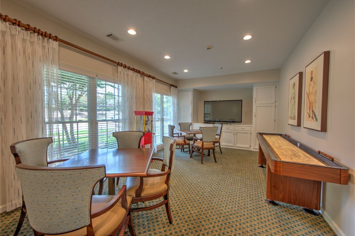 A well-lit conference room with a large table, surrounded by chairs, featuring a TV, shuffleboard table, and large windows.