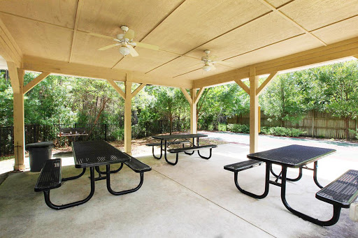 A spacious outdoor pavilion featuring picnic tables and ceiling fans, surrounded by greenery.