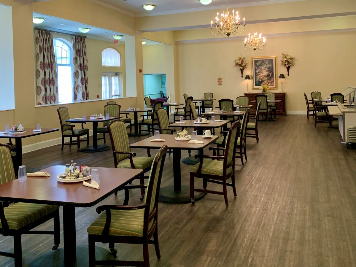An elegant dining room setup with neatly arranged tables and chairs, illuminated by chandeliers.