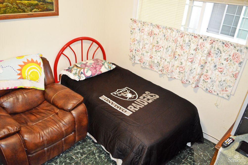 A cozy bedroom featuring a single bed with a Raiders blanket, a red headboard, and a leather chair beside it.