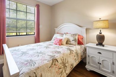A cozy bedroom with a floral bedspread, white headboard, and a warm lamp on the nightstand.