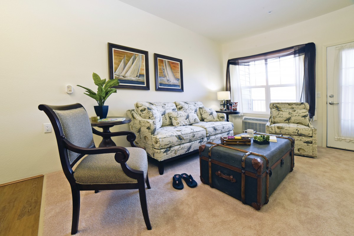 A cozy living room with floral-patterned furniture, a trunk-style coffee table, and decorative elements like plants and artwork.