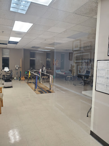 A view of a rehabilitation gym featuring exercise equipment and a glass partition.