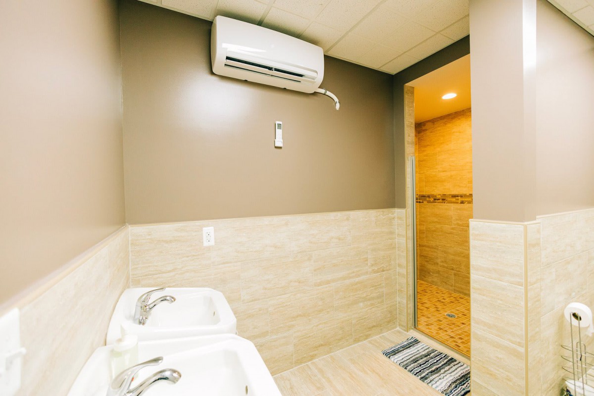 A modern bathroom with twin sinks and an air conditioning unit.