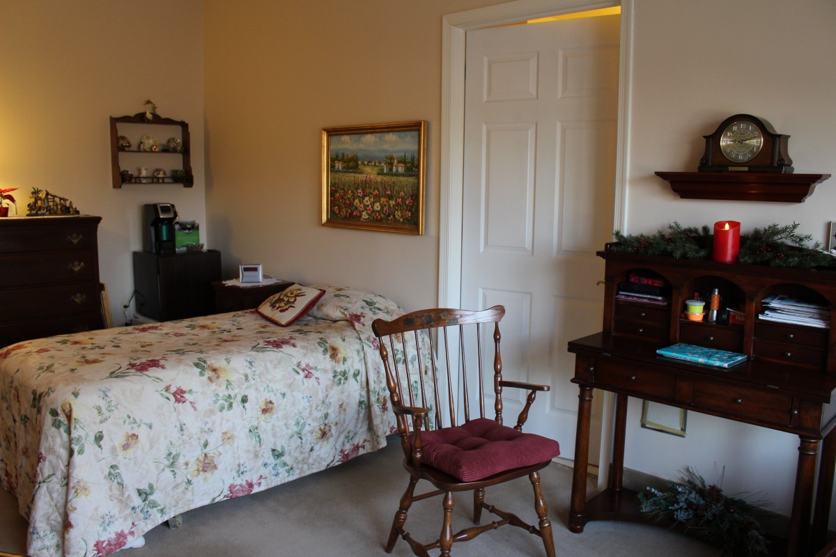 A cozy bedroom with a wooden chair, desk, and a bed adorned with floral bedding.