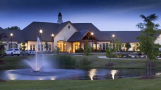 A well-lit building by a water feature with fountains and reflections at night.