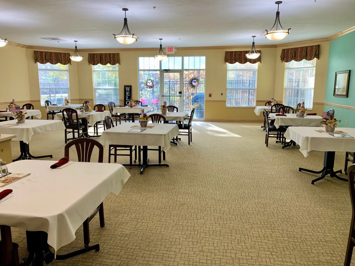 Spacious dining area with neatly arranged tables and chairs, illuminated by natural light from large windows.
