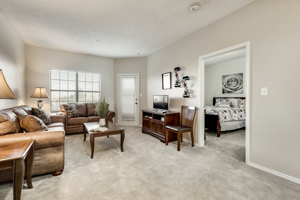 A cozy living room with a brown leather sofa, coffee table, and television stand, featuring a view into the adjacent bedroom.