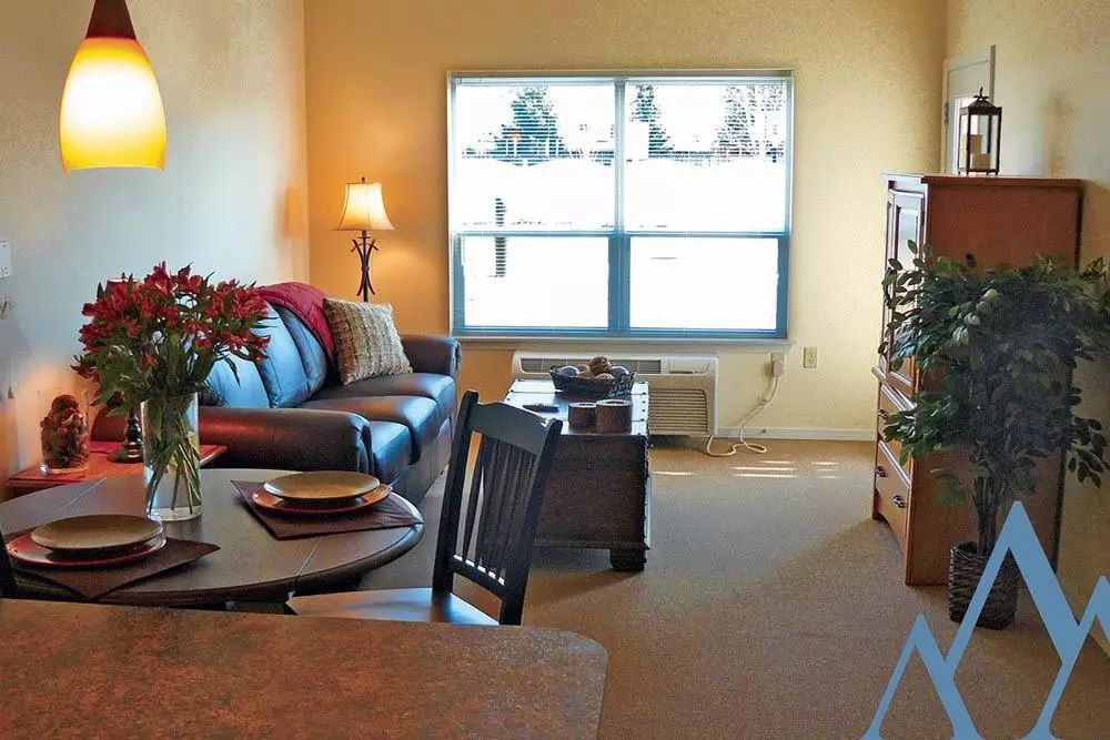 A cozy living room with a sofa, lamp, and table near a large window.