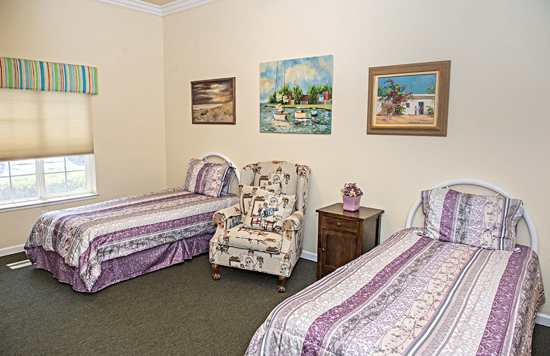 A cozy bedroom with two twin beds, decorated with floral patterns and paintings on the wall.
