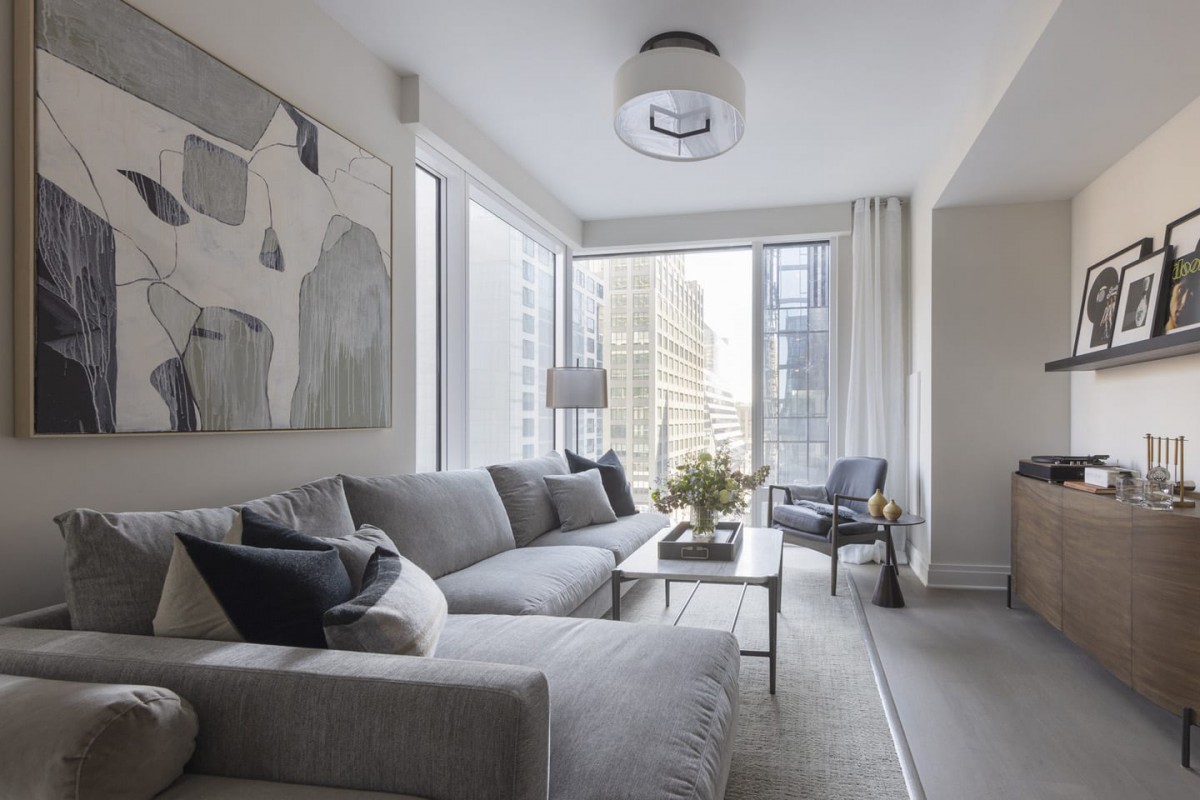 A modern living room with a gray sofa and large windows showcasing a city view.