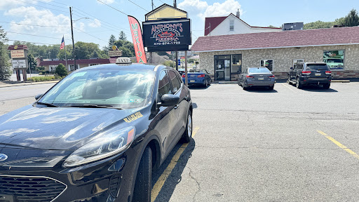 A black taxi is parked outside a restaurant with visible signage in a sunny urban setting.