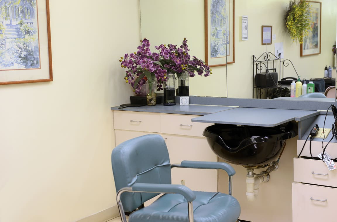 A salon interior with a styling chair, mirror, and flowers on the counter.