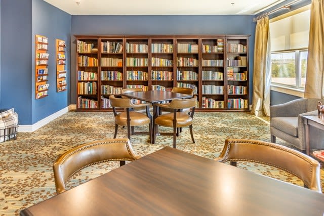 A cozy library room with wooden bookshelves, a table surrounded by chairs, and a decorative carpet.