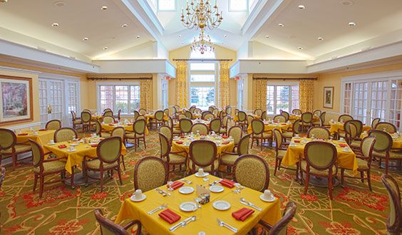 A spacious and elegantly decorated dining room with multiple tables set for dining, featuring yellow tablecloths and a chandelier overhead.