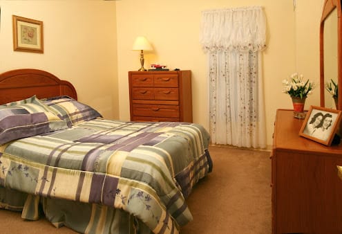 A cozy bedroom with a bed, dresser, and a lamp.