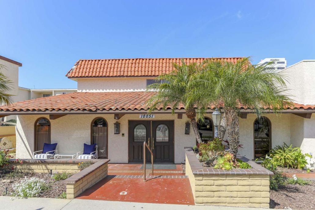 A Spanish-style residential house with a tile roof and palm trees, featuring a landscaped front area.