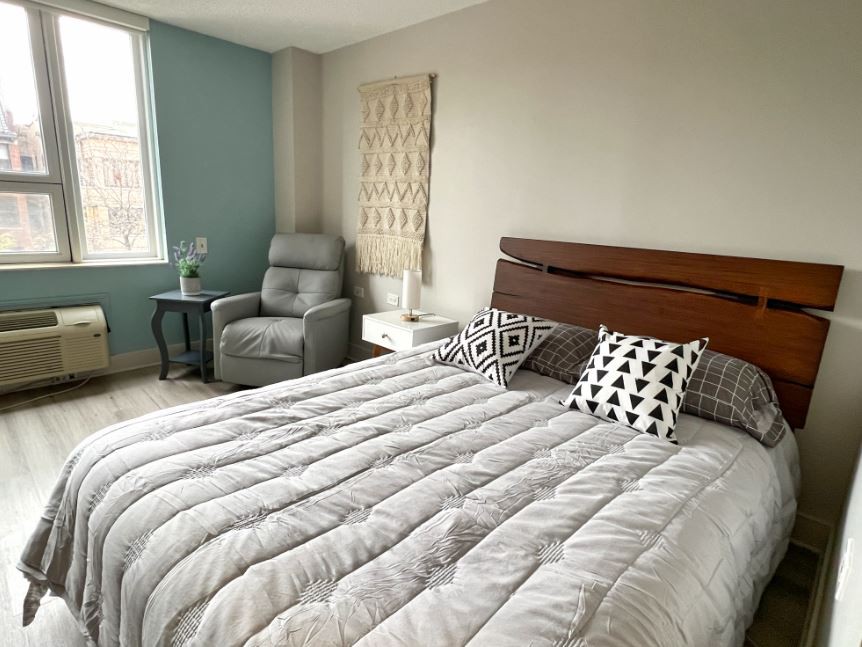 A modern and minimalist bedroom with a comfortable bed, stylish pillows, and an armchair by the window.