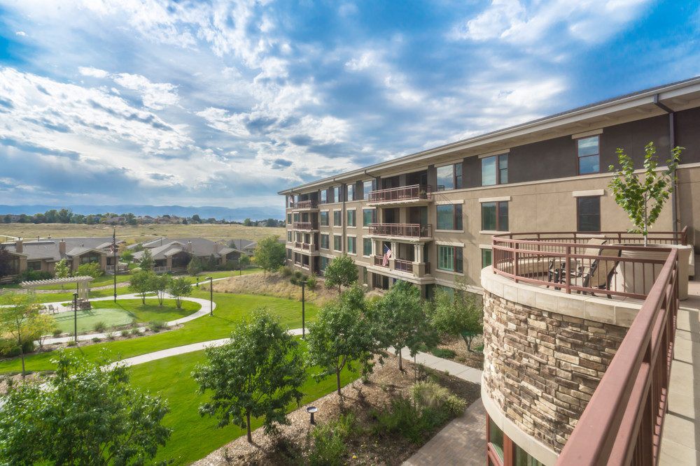 A scenic view of a modern apartment complex surrounded by lush greenery and under a partly cloudy sky.
