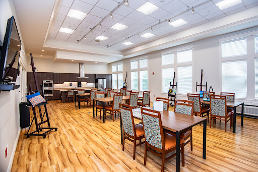 A spacious and modern dining area featuring tables and chairs arranged neatly, illuminated by natural light.