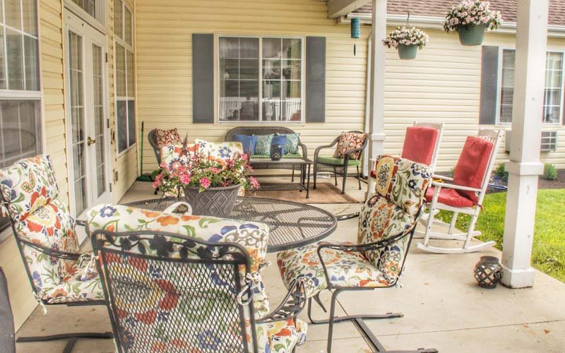 A cozy outdoor patio area with various chairs and a table, featuring colorful cushions and a hanging flower pot.