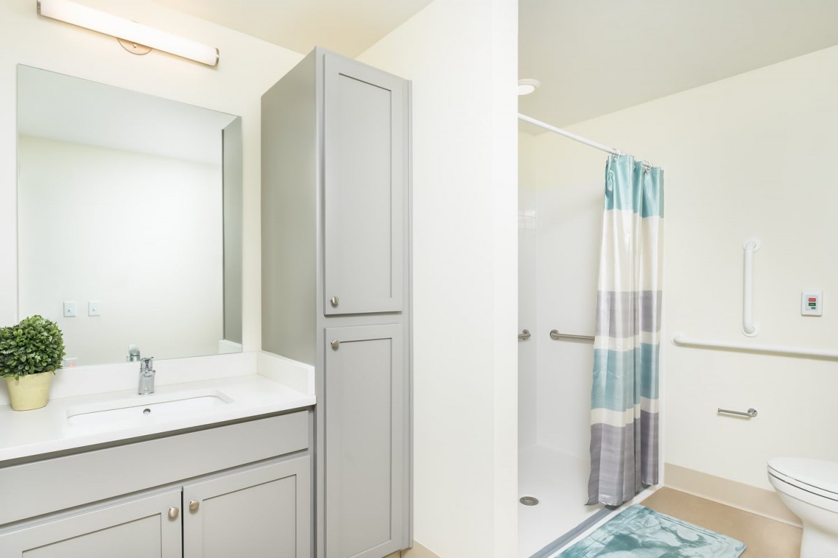 A modern bathroom featuring a shower with a striped curtain, a sink with cabinetry, and ample storage space.