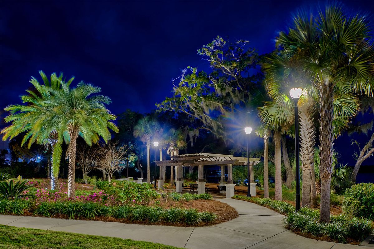 A beautifully lit park at night with a gazebo and palm trees lining the pathway.