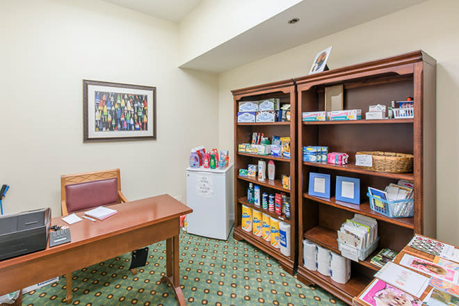 An office space with a desk, bookshelves filled with supplies, and a small refrigerator.