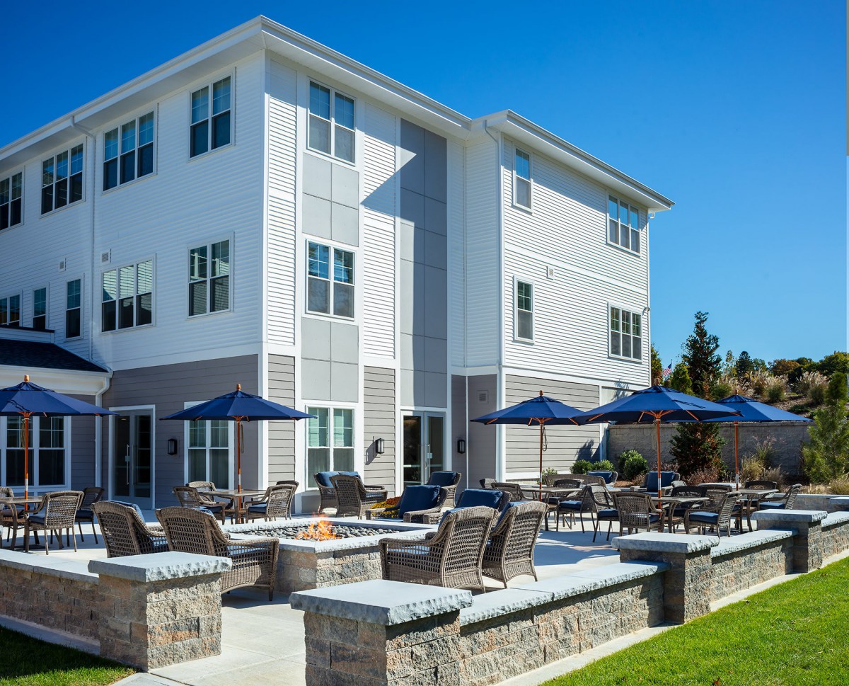 A modern residential building with outdoor seating and umbrellas on the patio.