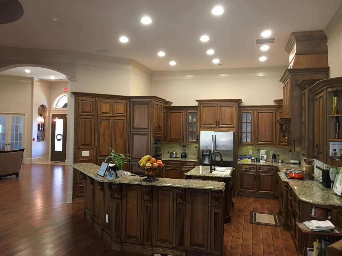 A spacious kitchen with wooden cabinets and a large island, featuring stainless steel appliances and recessed lighting.