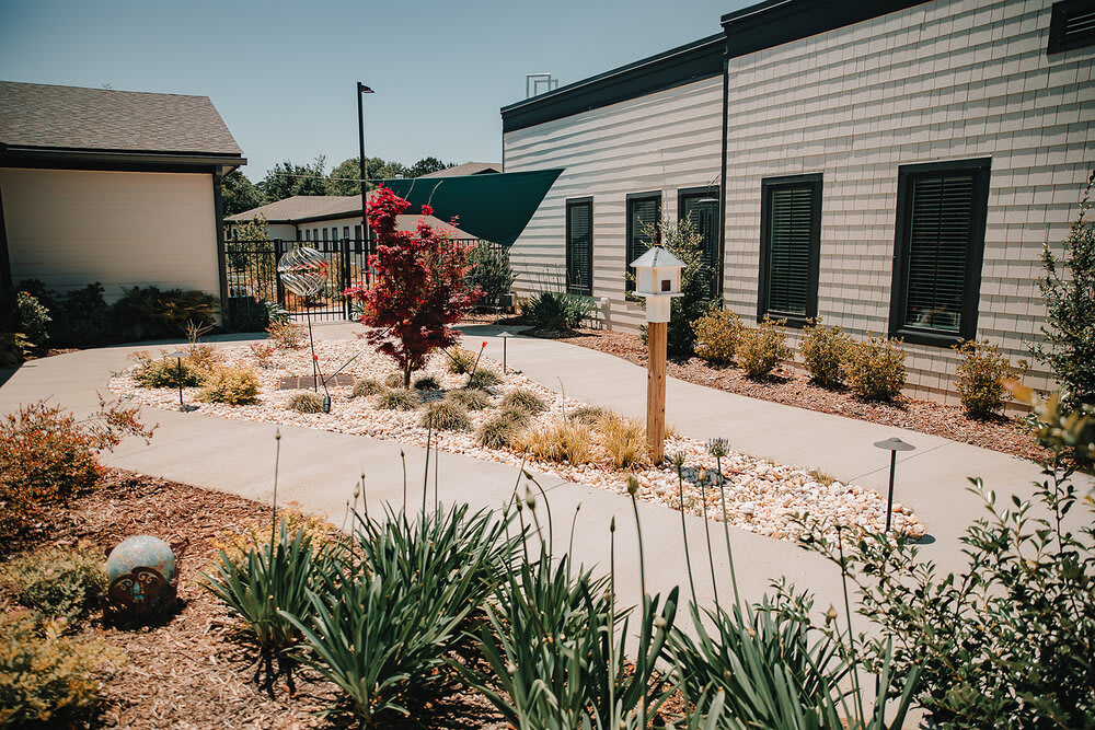 A well-maintained garden pathway featuring diverse plants and decorative yard art beside a modern building.