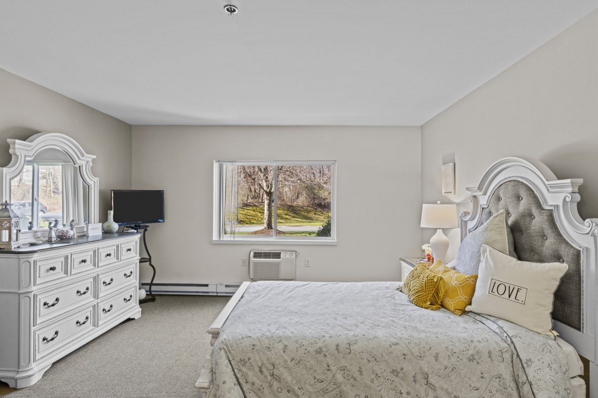 A cozy bedroom with neutral tones featuring a bed, dresser, and window view.