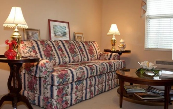 A cozy living room with a floral patterned sofa, lamp, and artwork on the walls.