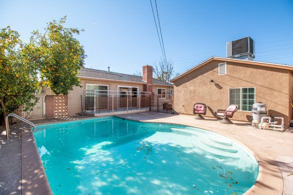 A sunny backyard featuring a swimming pool with patio chairs nearby.