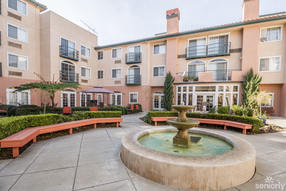 A serene courtyard featuring a central fountain surrounded by benches and a multi-story residential building.