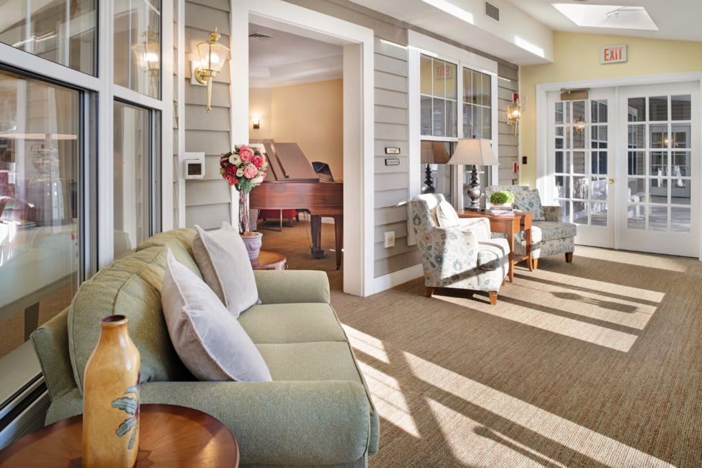 A cozy living room with a sofa, armchairs, and a piano, bathed in natural light.