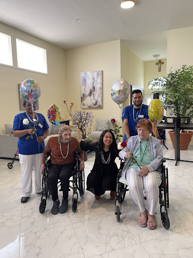 A joyful gathering featuring elderly residents and caregivers, celebrating with balloons and smiles in a warm indoor setting.