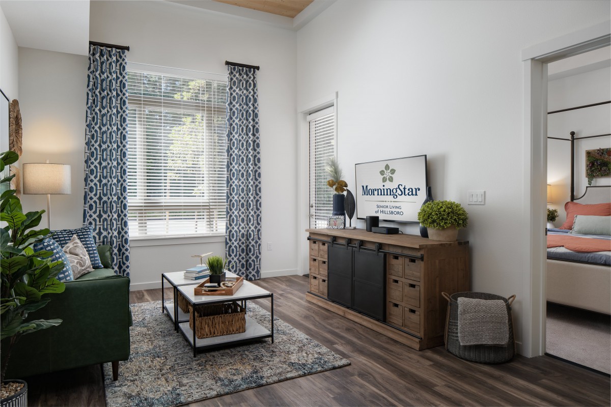 A modern living room with stylish decor, featuring a television on a wooden cabinet, a coffee table with plants, and elegant curtains.