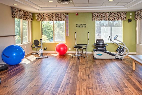 A well-lit gym room with various exercise equipment including an elliptical machine and an exercise ball.