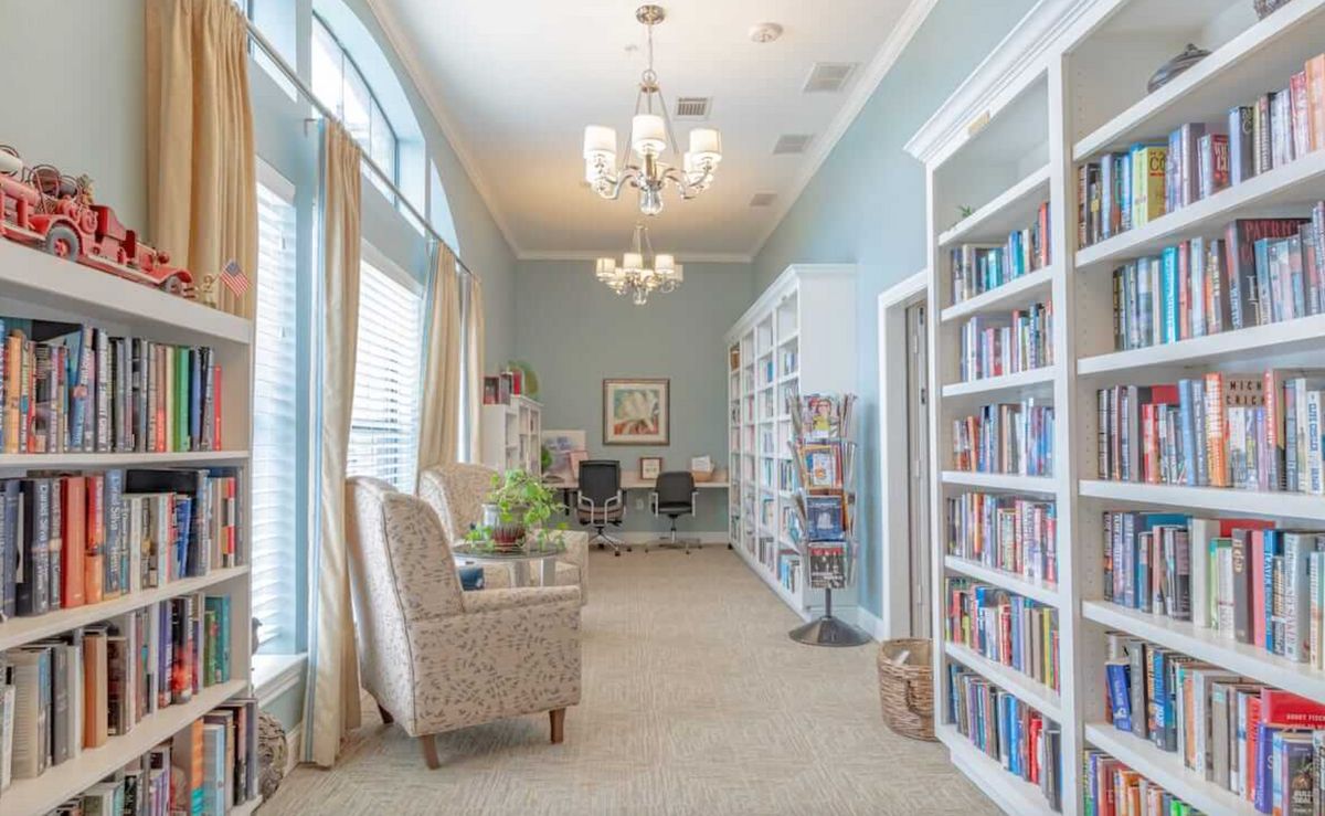 A cozy library with bookshelves, comfortable seating, and elegant chandeliers.