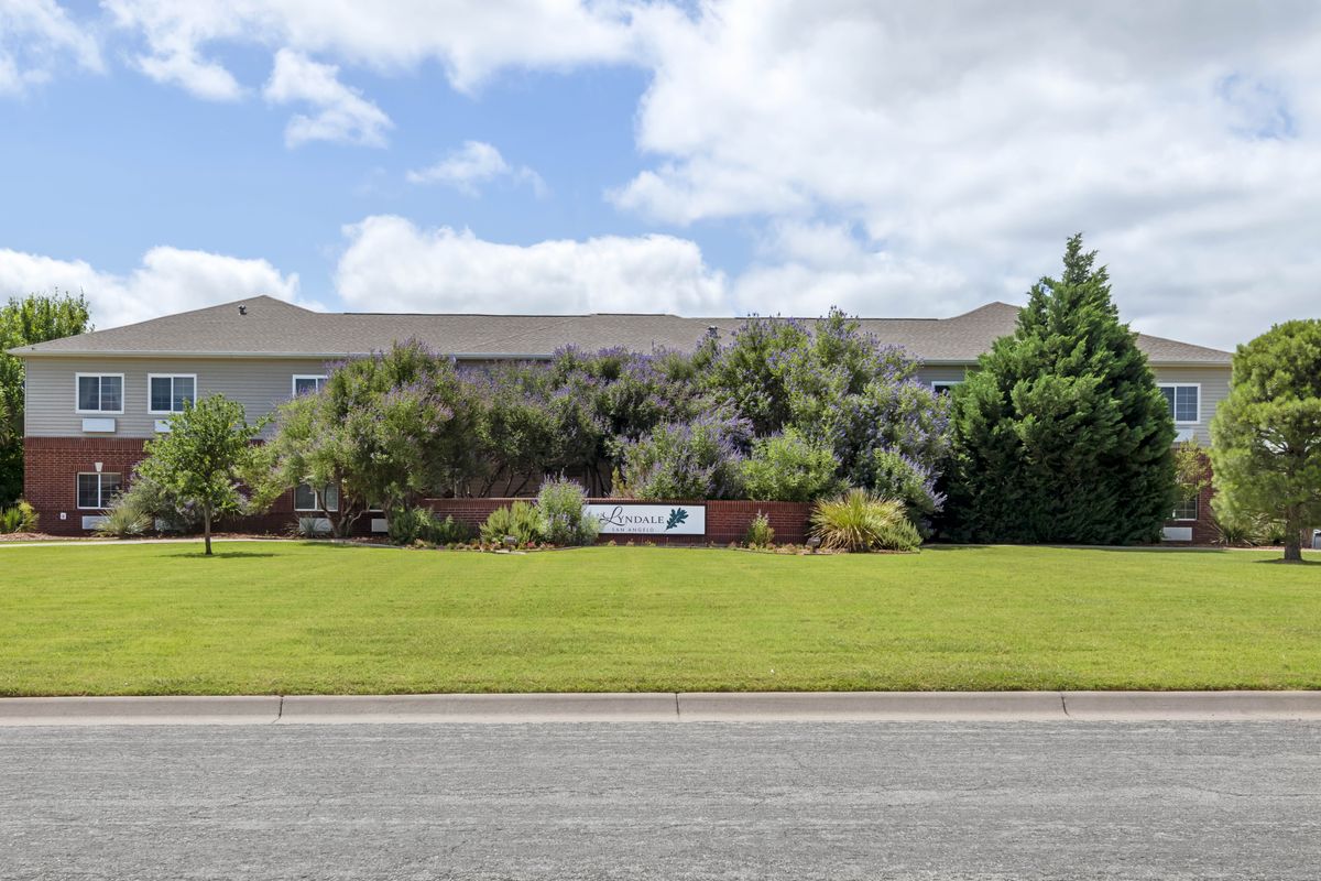 A building with a well-maintained lawn and a sign in front, surrounded by trees under a partly cloudy sky.