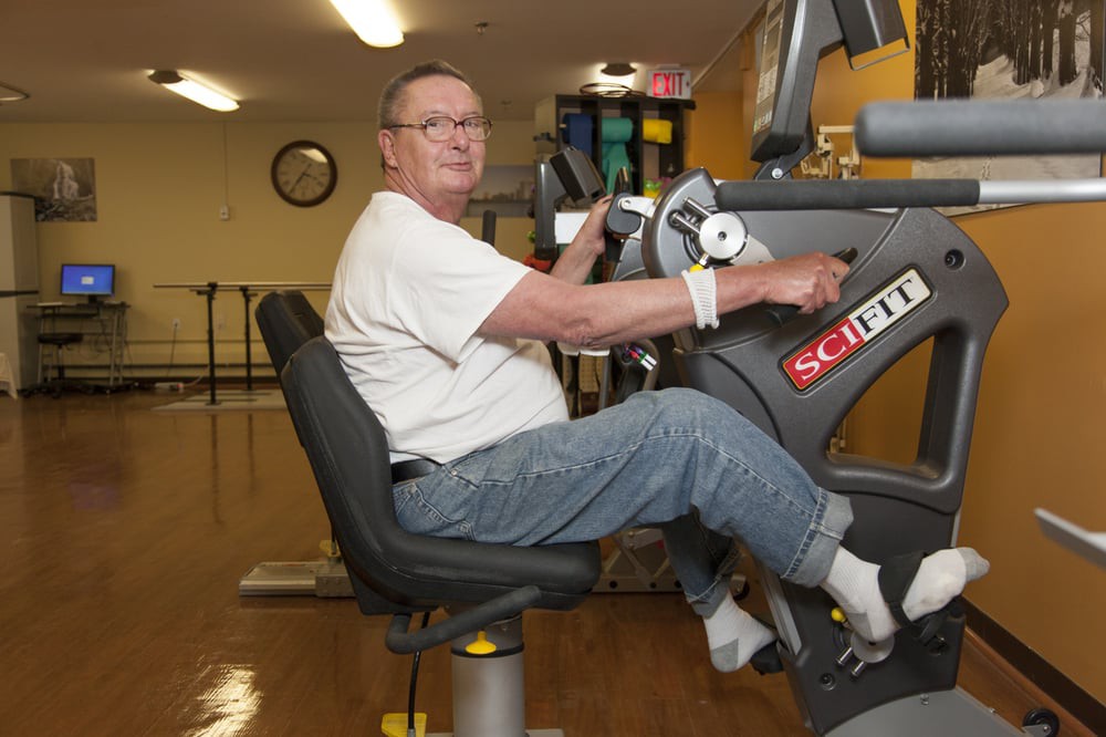 An elderly person is using exercise equipment indoors for rehabilitation and fitness.
