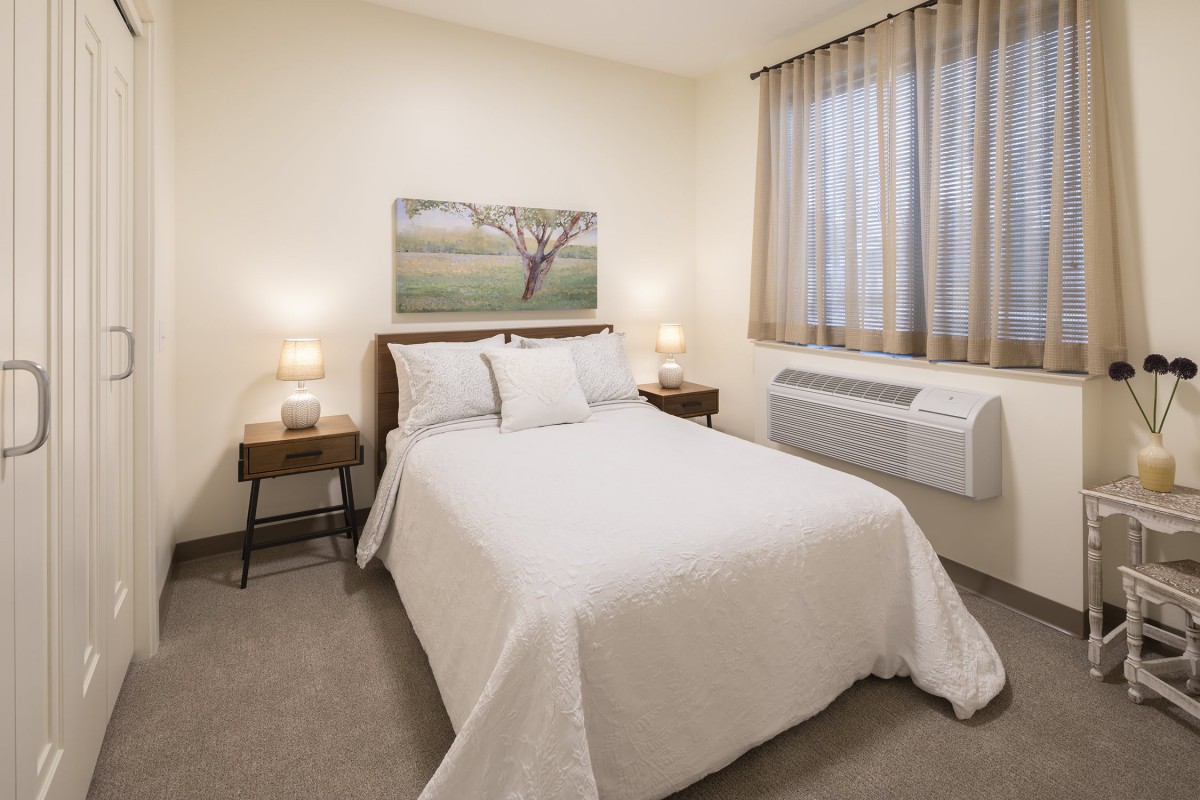A cozy and minimalist bedroom with a neatly made bed, bedside tables with lamps, and a window with curtains.