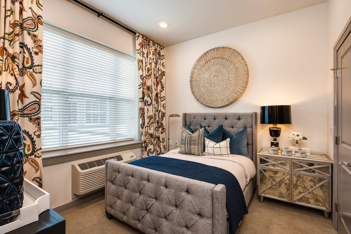 A stylishly decorated bedroom featuring a tufted bed, patterned curtains, and decorative wall art.