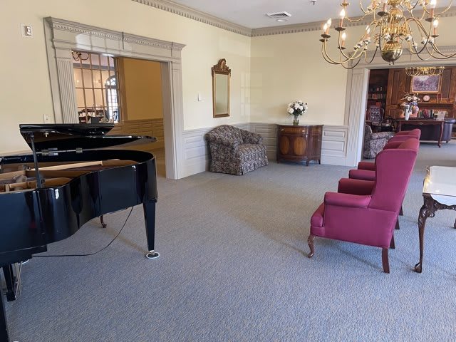 A well-furnished waiting room featuring a grand piano, upholstered chairs, and a chandelier.
