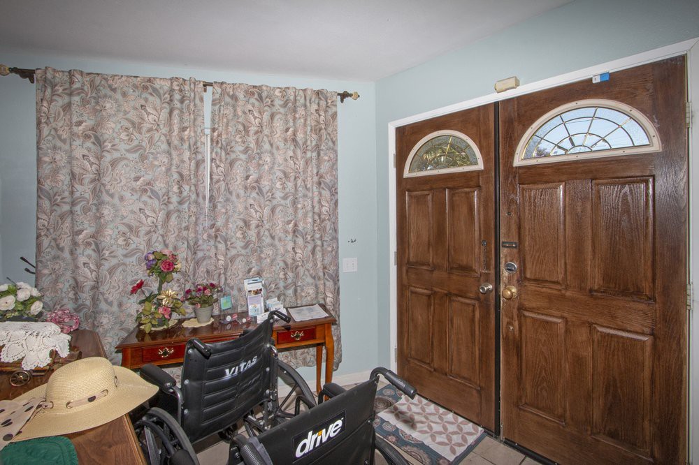 A cozy entryway featuring wooden double doors, a wheelchair, and decorative plants on a small table.