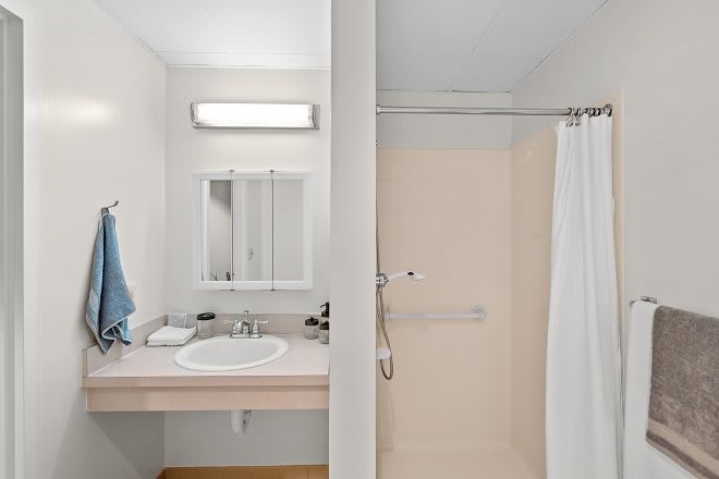 A clean and simple bathroom with a sink, mirror, and shower area.