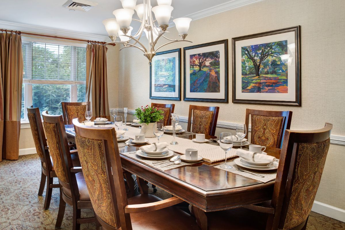 A well-appointed dining room featuring a large wooden table set for a meal, surrounded by matching chairs, with a chandelier hanging overhead and framed artwork on the walls.