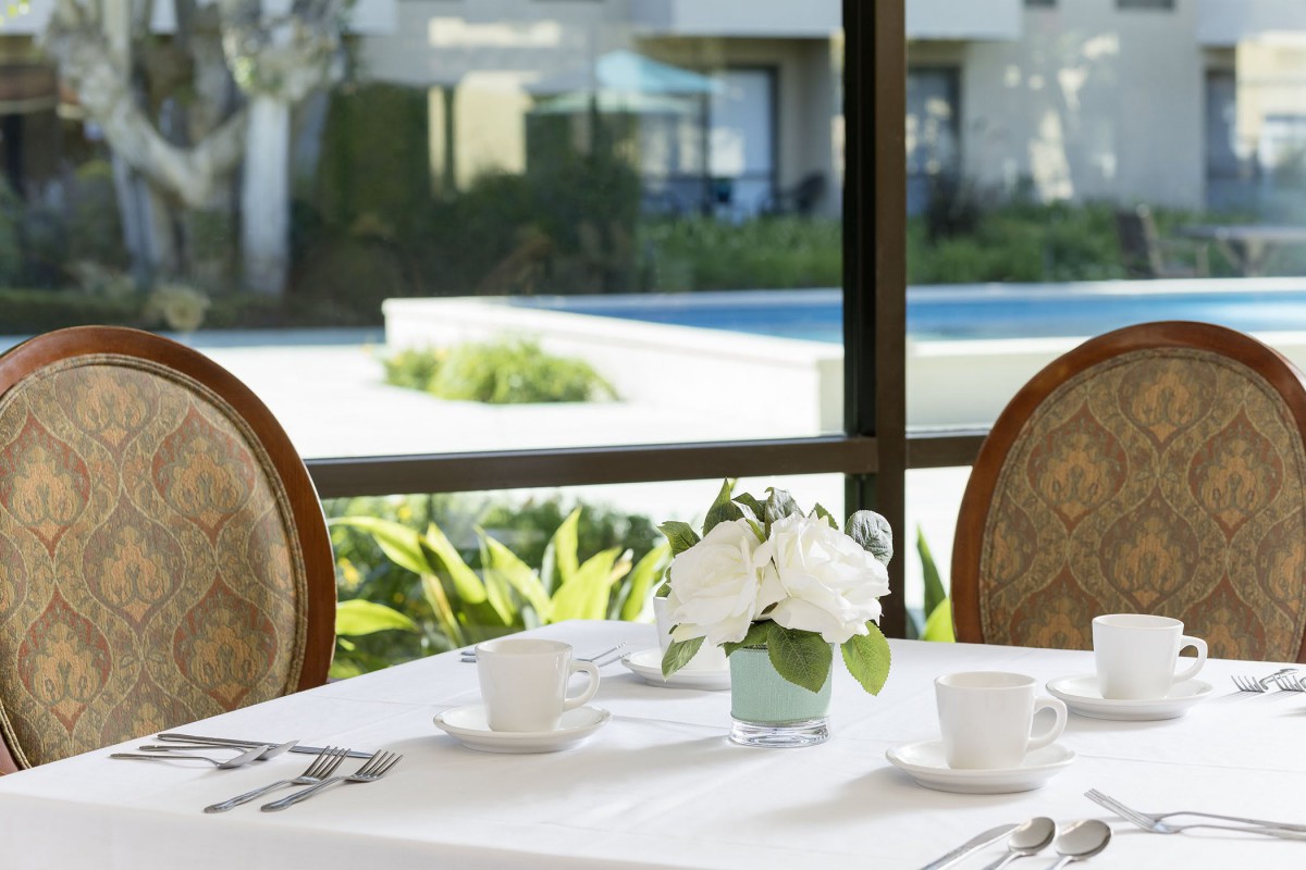 A dining table set with white dishes and a floral centerpiece, positioned near a window with a view outside.