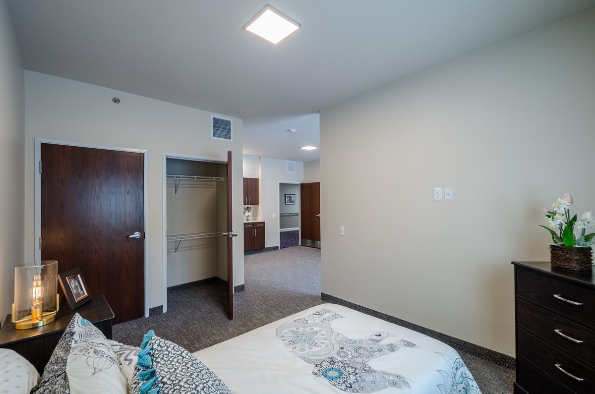 A modern bedroom with an open closet and view into the kitchen area.